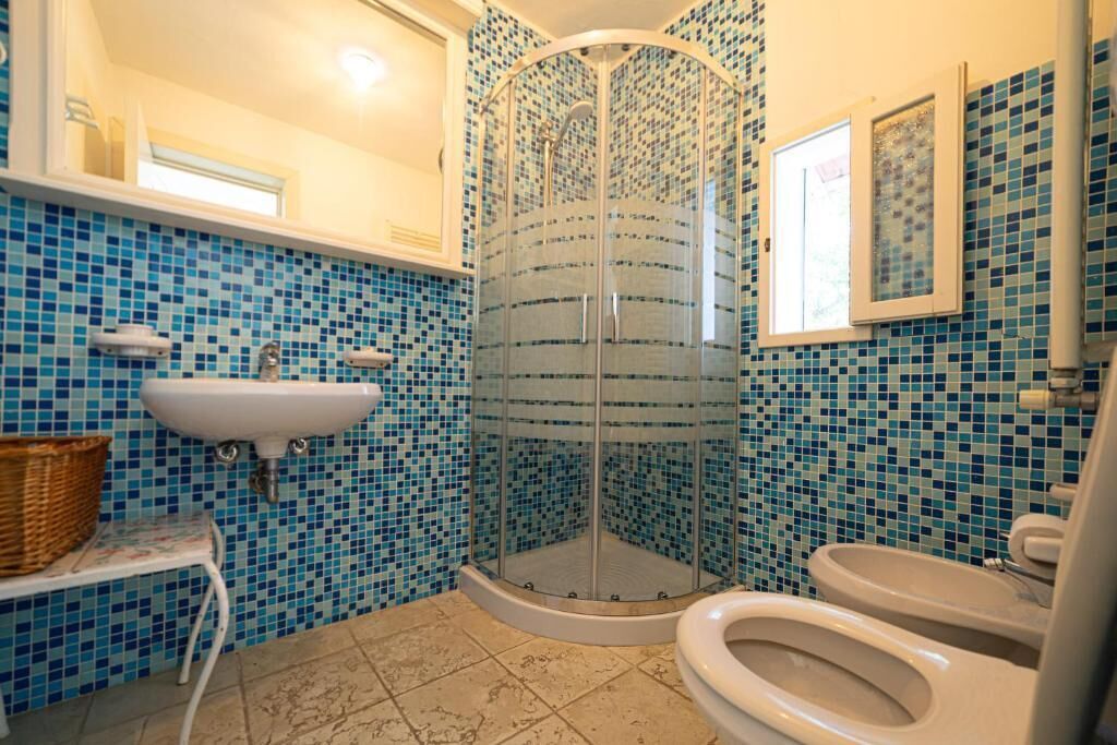A bathroom with a glass shower enclosure, a sink, and two toilets.