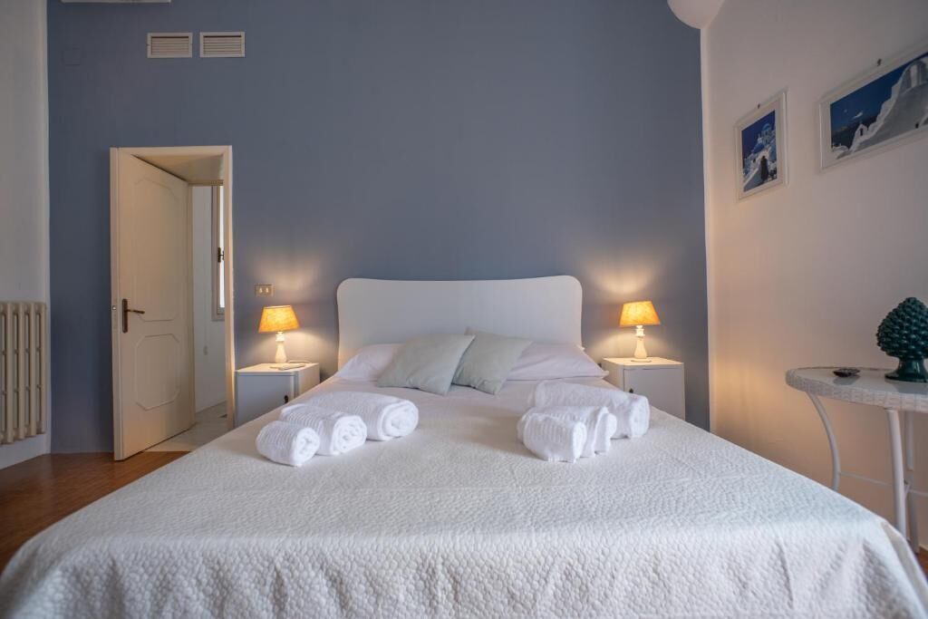 Una cama bien hecha con sábanas y toallas blancas, dos lámparas de noche y una mesita con una decoración de piña.