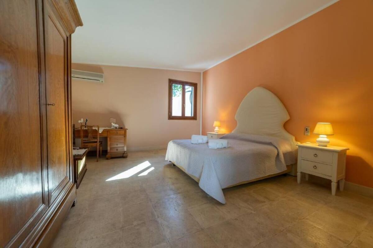 Een slaapkamer met een bed, nachtkastjes, een kledingkast, een bureau en een raam.