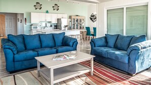 Ein Wohnzimmer mit zwei blauen Sofas, einem Couchtisch und einer Küche im Hintergrund.