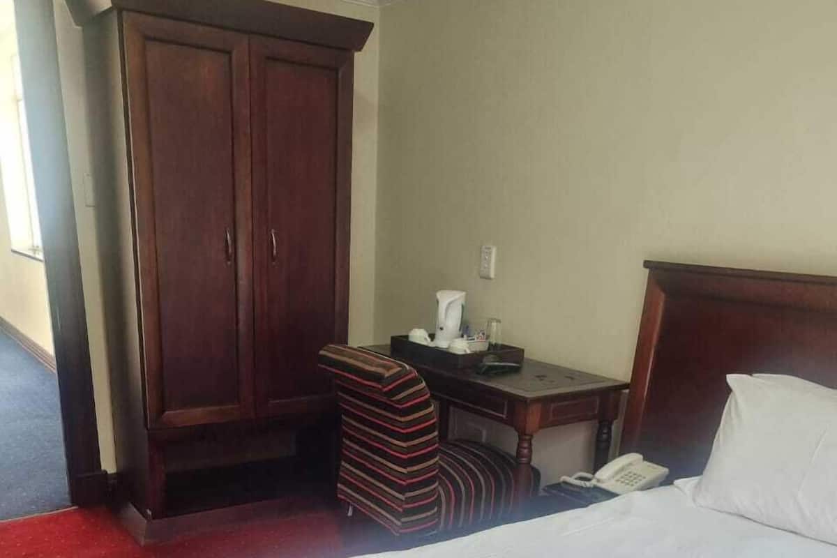 A hotel room with a large bed, a wooden wardrobe, a small desk with a telephone, and a striped chair.