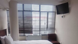 Une chambre d’hôtel avec deux lits, un téléviseur à écran plat fixé au mur et une fenêtre avec des stores.