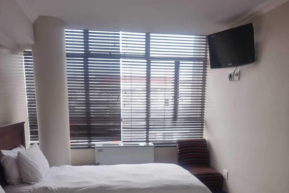 A hotel room with two beds, a flat-screen TV mounted on the wall, and a window with blinds.
