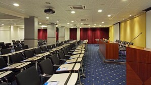 Une salle de conférence avec des rangées de bureaux, un pupitre et une scène avec des rideaux.