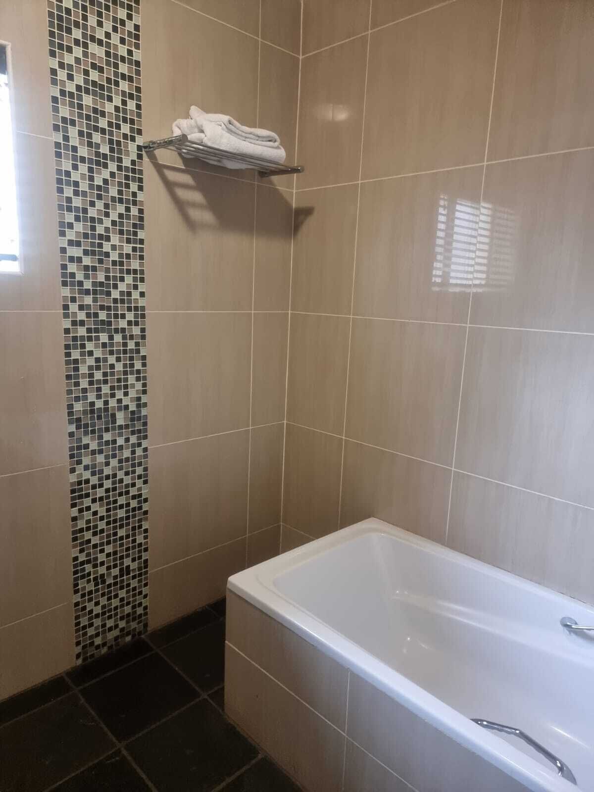 A bathroom with a tiled wall, a white bathtub, and a towel rack.