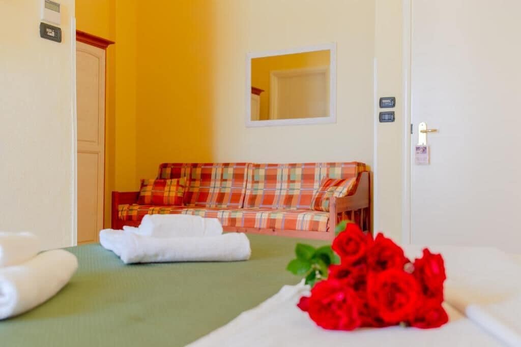 A hotel room with a bed, a sofa, a mirror, and a bouquet of red roses.