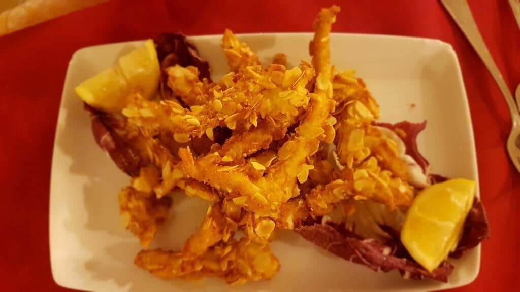 Ein weißer Teller mit gebratenem Essen und Zitronenspalten auf einer roten Tischdecke.