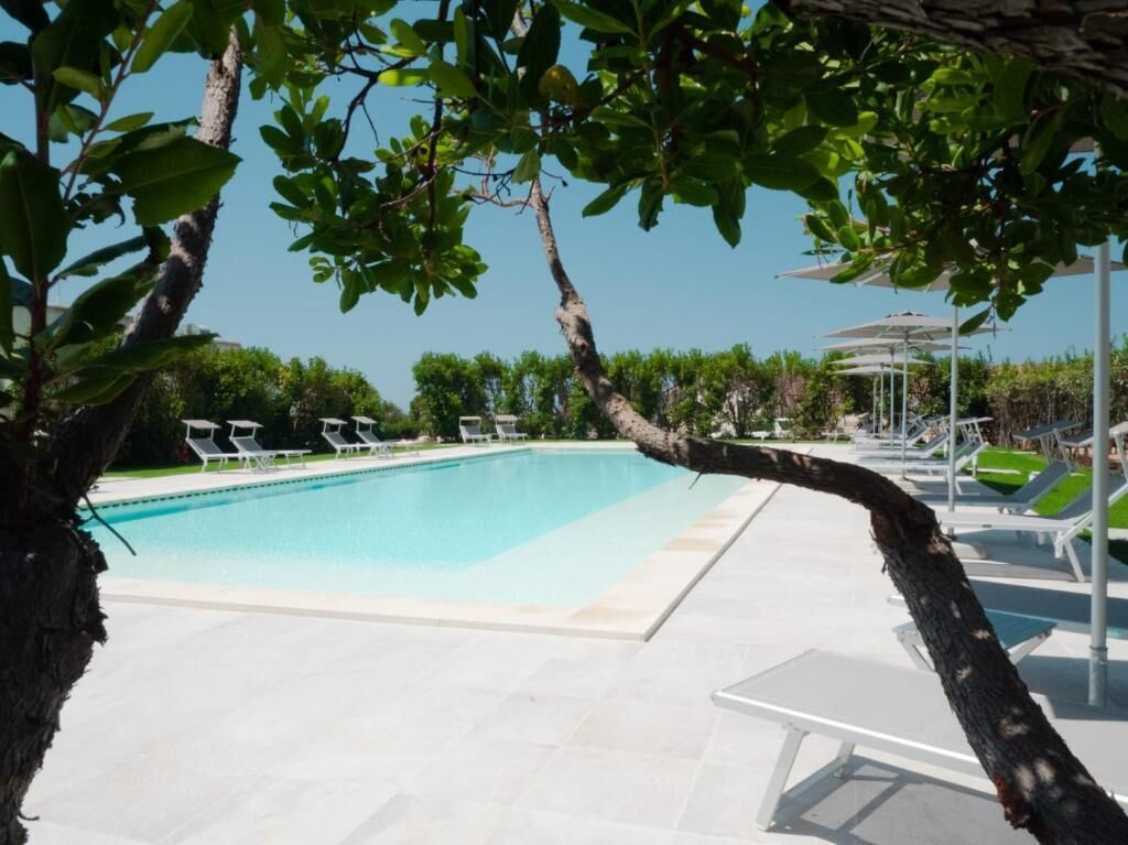A swimming pool with lounge chairs and umbrellas, surrounded by trees and a clear sky.