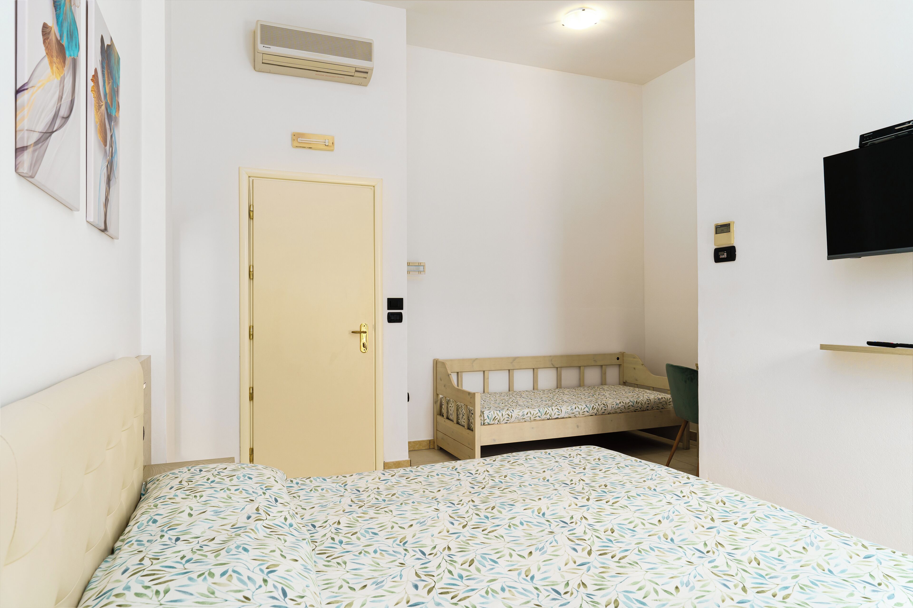 Une chambre à coucher avec un lit, une table de chevet, une chaise, une porte et un téléviseur fixé au mur.