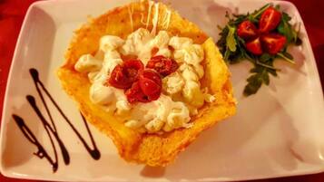 Een vierkant bord met een dessert, afgetopt met slagroom en rode vruchten, vergezeld van een kleine salade en chocoladesiroop.