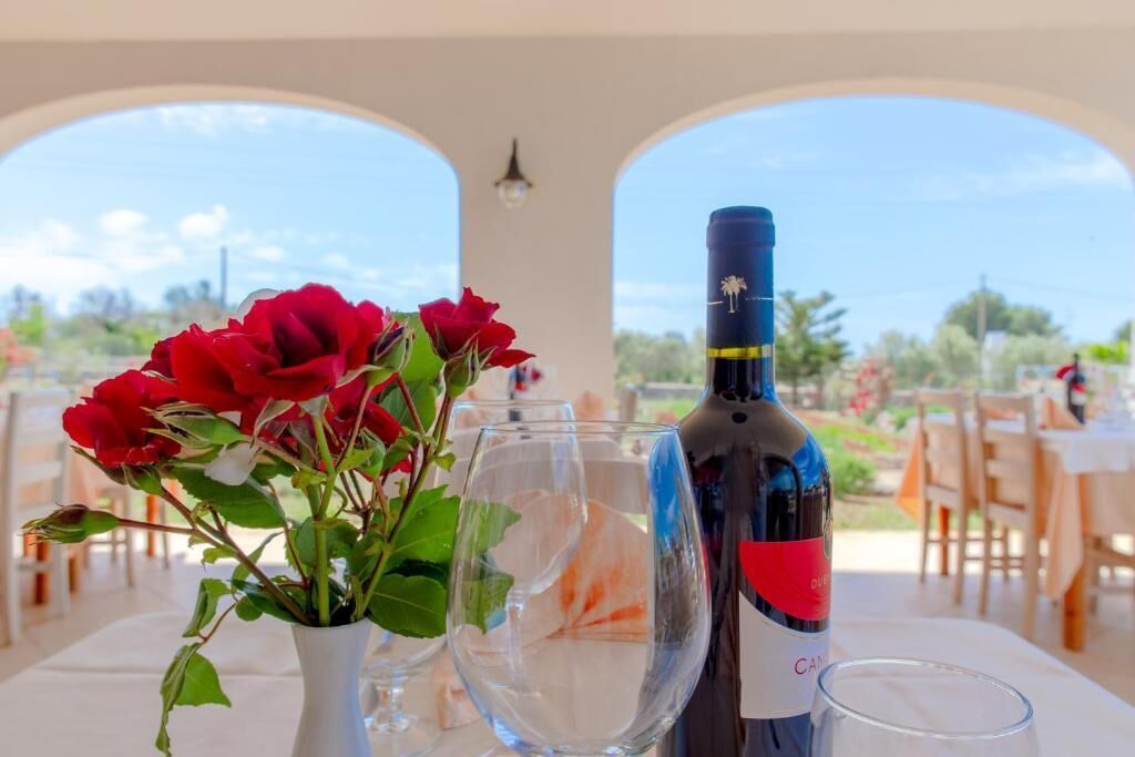 A table with a bottle of wine, a glass, and a vase with red roses.