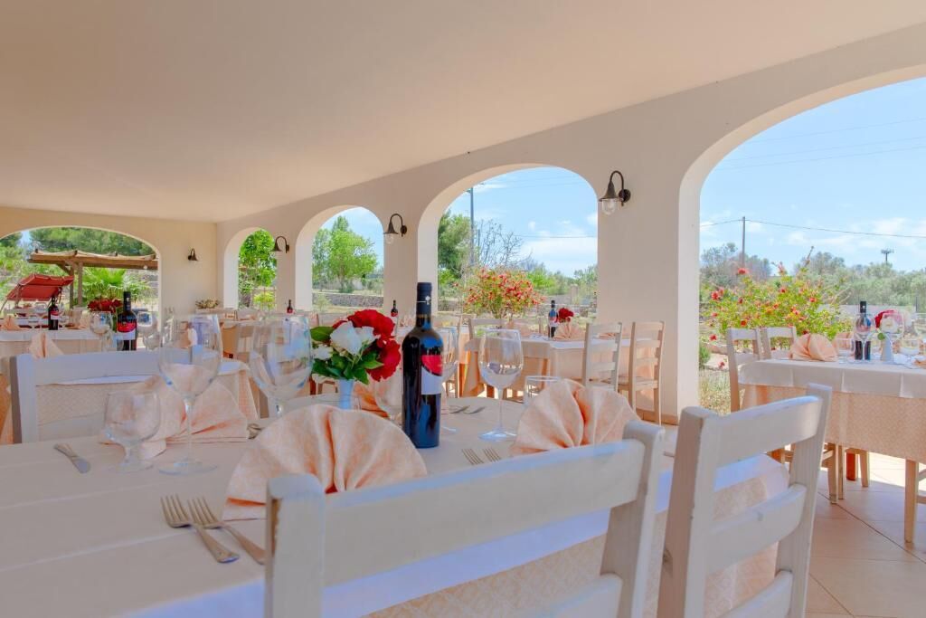 Un restaurante con mesas y sillas blancas, frente a un fondo de vegetación y cielo despejado.