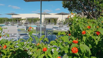 Un espace aménagé au bord de la piscine, avec des chaises longues et des parasols, entouré de verdure et de fleurs.