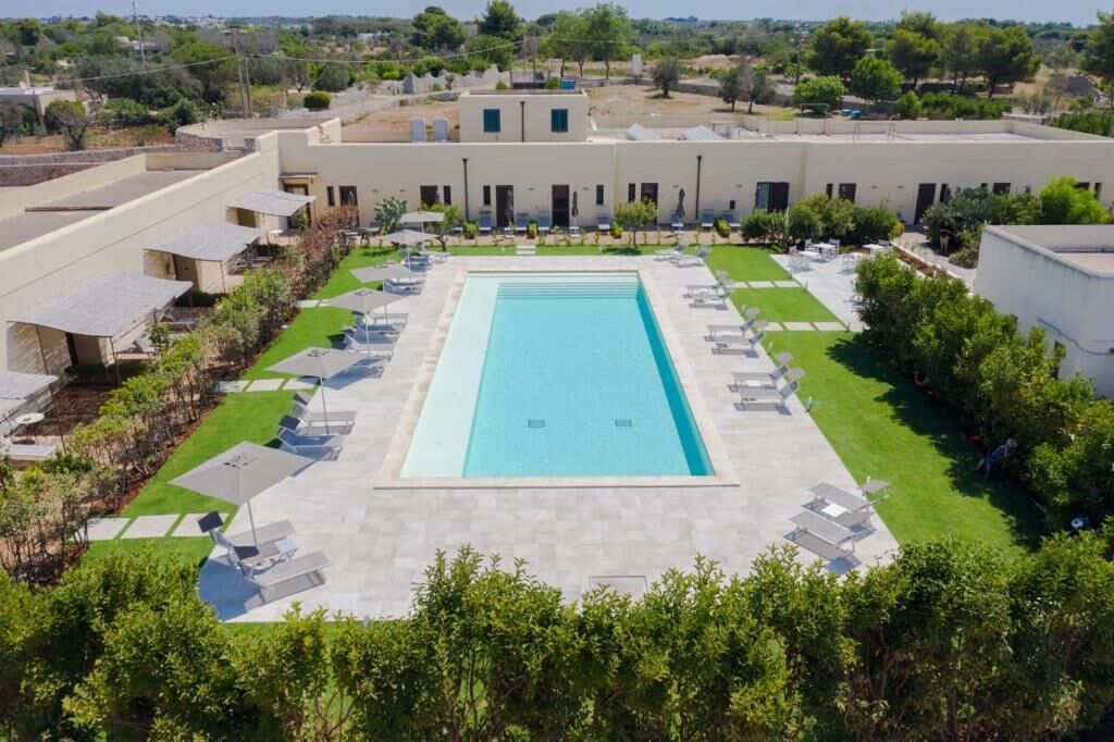 A rectangular swimming pool surrounded by lounge chairs and a lawn area.
