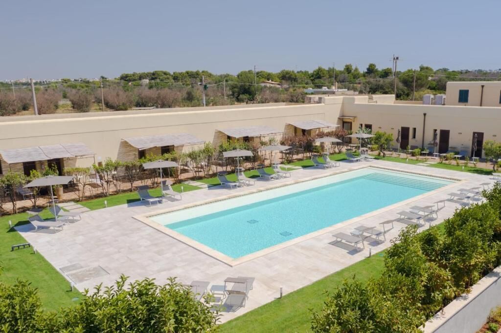 A swimming pool with lounge chairs and small huts, surrounded by greenery.