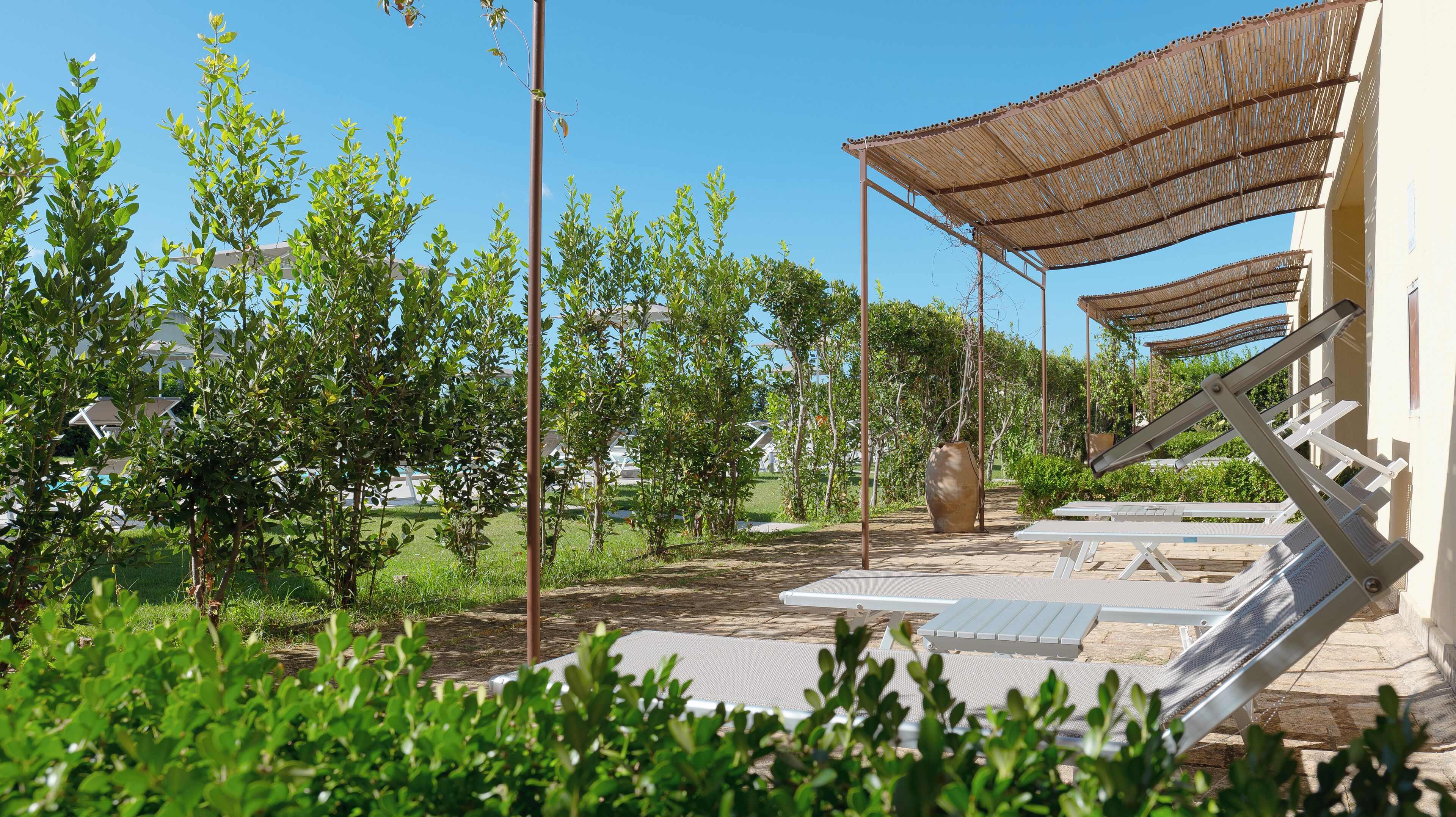 An outdoor area with a pergola, lounge chairs, and a large vase.