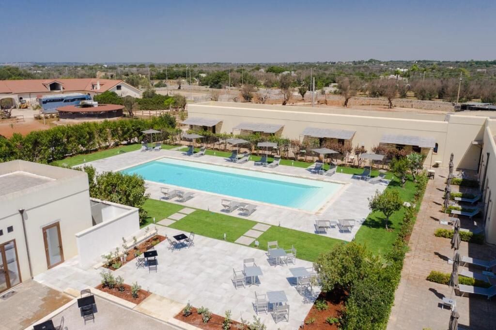 Una piscina con sillas de descanso y sombrillas, rodeada de vegetación y edificios.