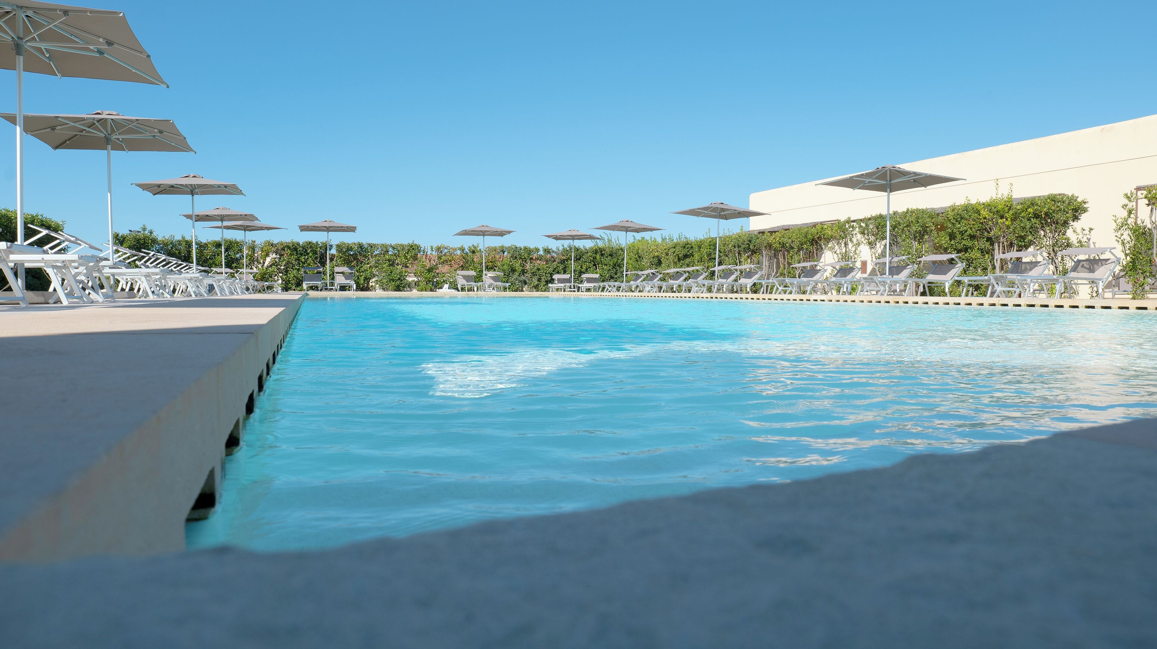 Ein Pool mit mehreren Liegestühlen und Sonnenschirmen, umgeben von Grünflächen und einem Gebäude.