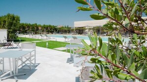 Ein Poolbereich mit Liegestühlen und einem Tisch, einem strahlend blauen Himmel und einem Gebäude im Hintergrund.