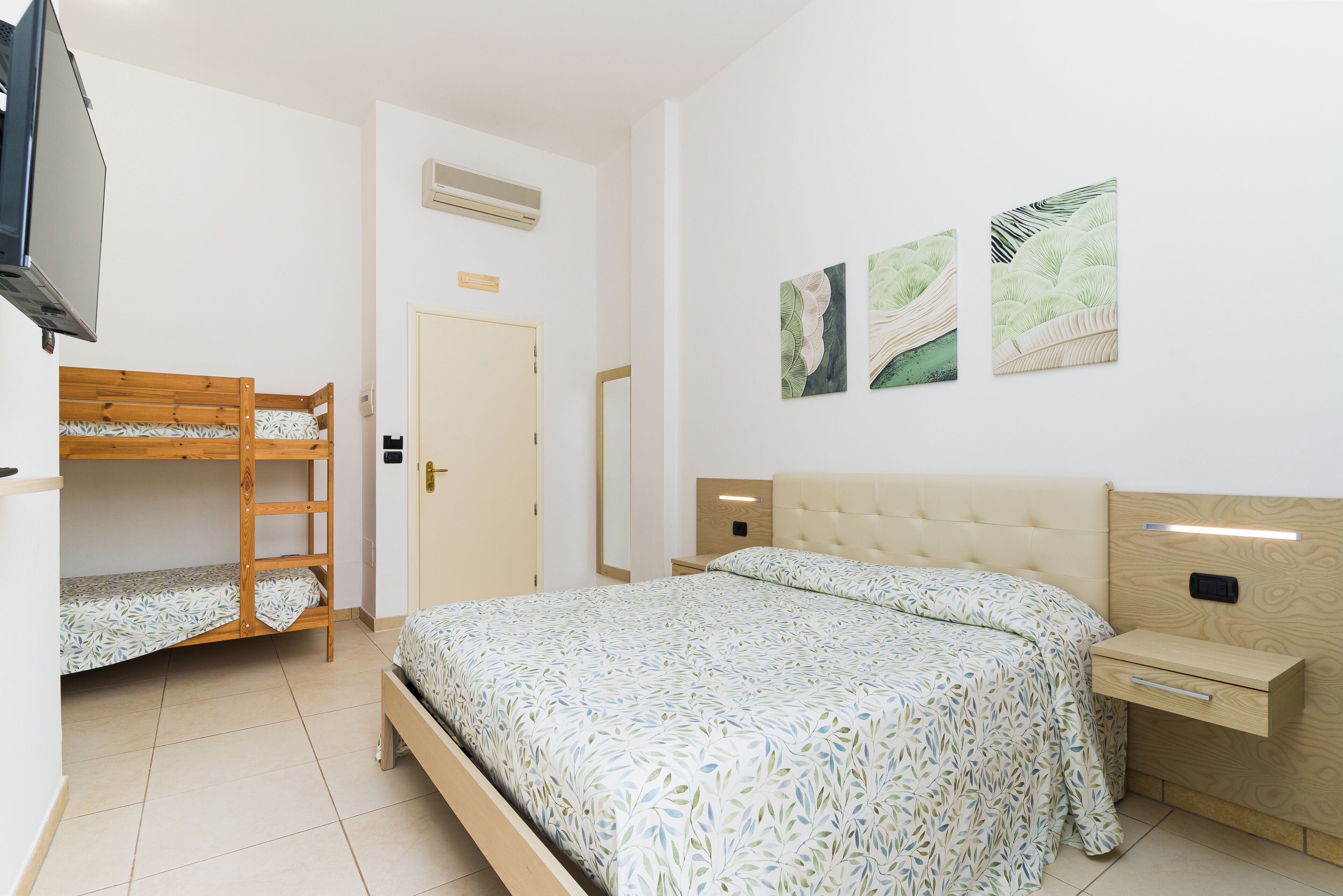 Une chambre avec un lit superposé, un lit simple, une table de chevet avec une lampe et des œuvres d’art murales.
