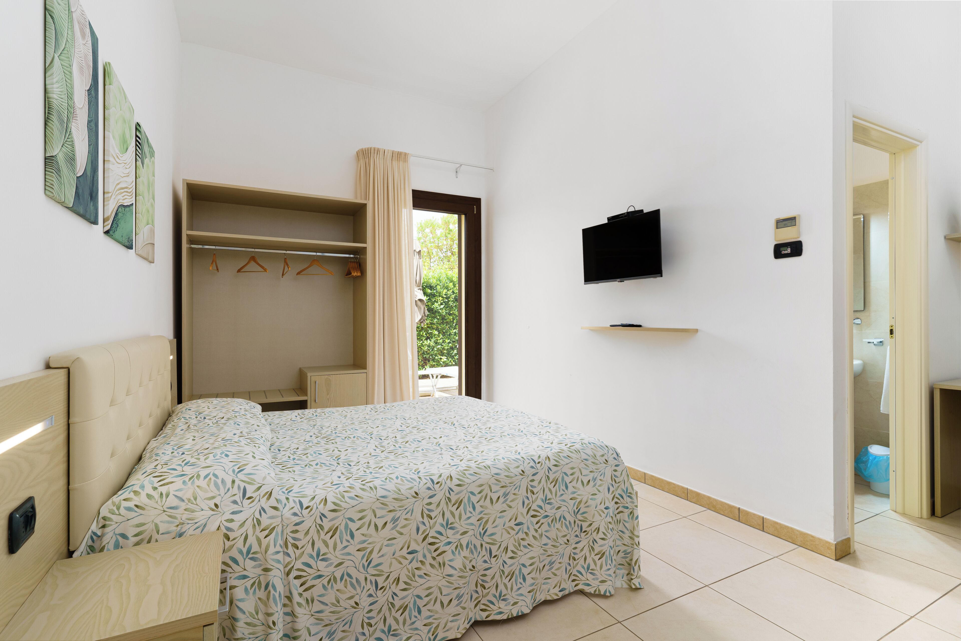 Une chambre à coucher comprenant un lit, une armoire, un téléviseur et une salle de bain visible à travers une porte ouverte.