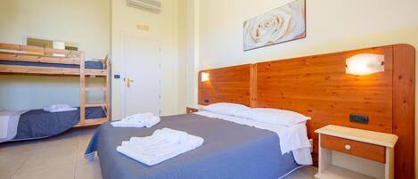 A room with a large bed, a smaller bunk bed, a bedside table, and a wall-mounted light fixture.