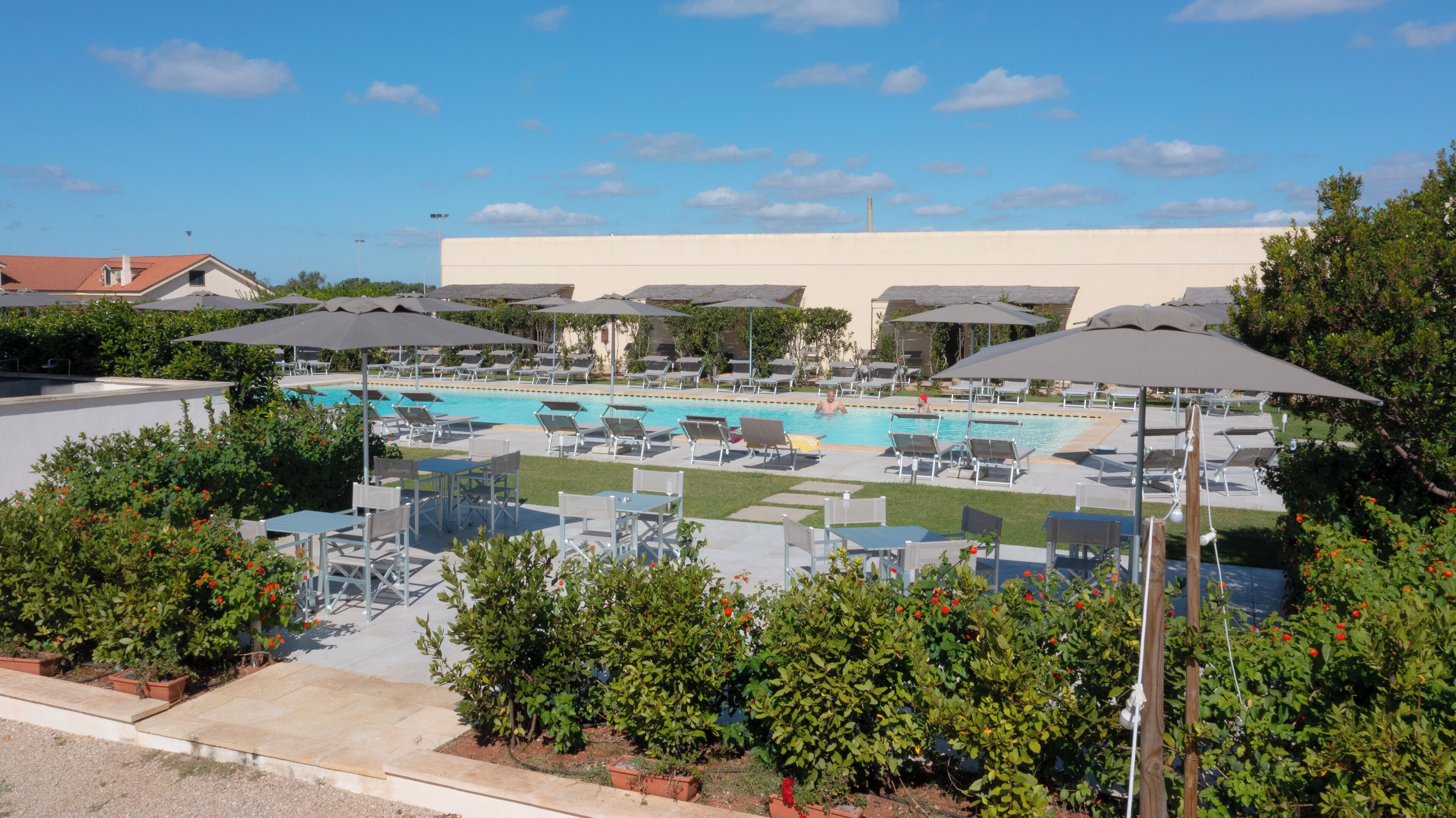 Zona de piscina con varias sillas de descanso y sombrillas, rodeada de vegetación.