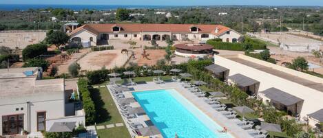 A large swimming pool with sun loungers and umbrellas, surrounded by a landscaped area with a view of the sea.