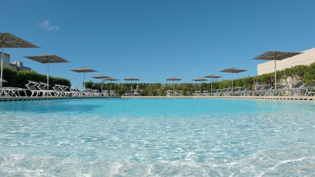 Ein Schwimmbecken mit klarem, blauem Wasser, umgeben von Liegestühlen und Sonnenschirmen.