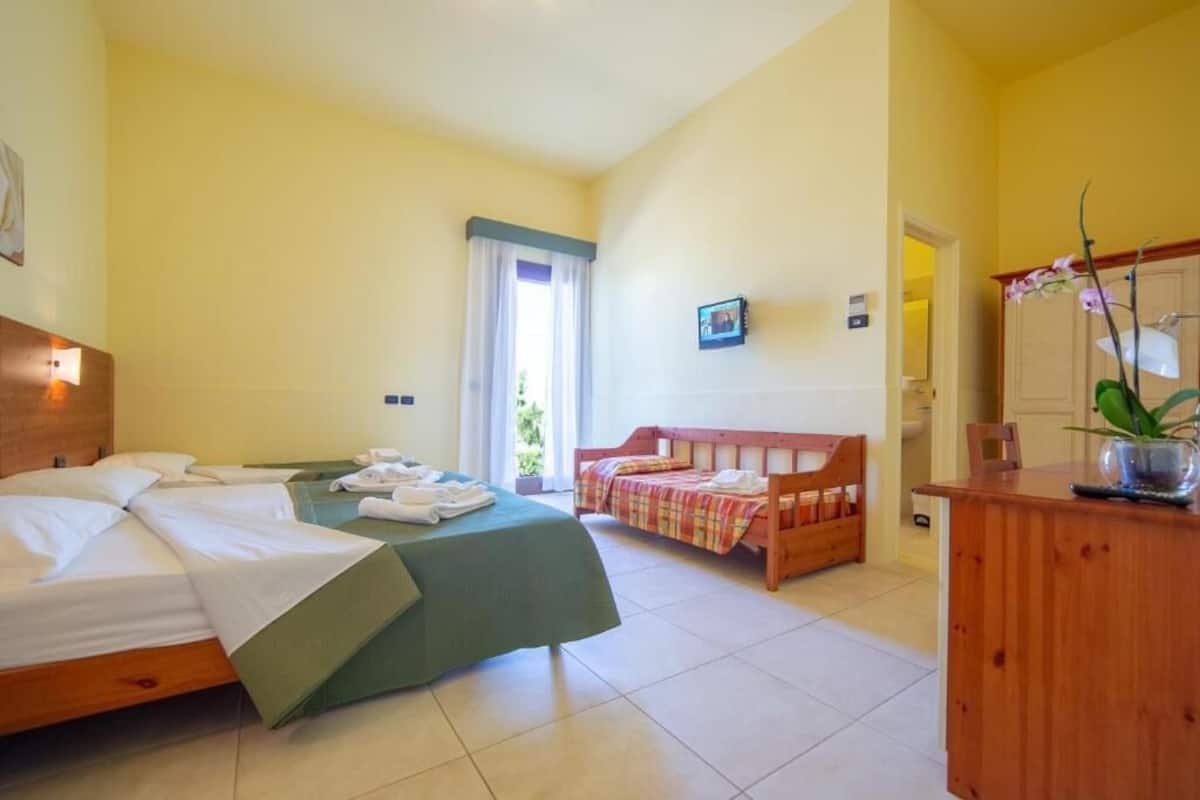 A hotel room with two beds, a wooden desk, a mirror, and a window with curtains.