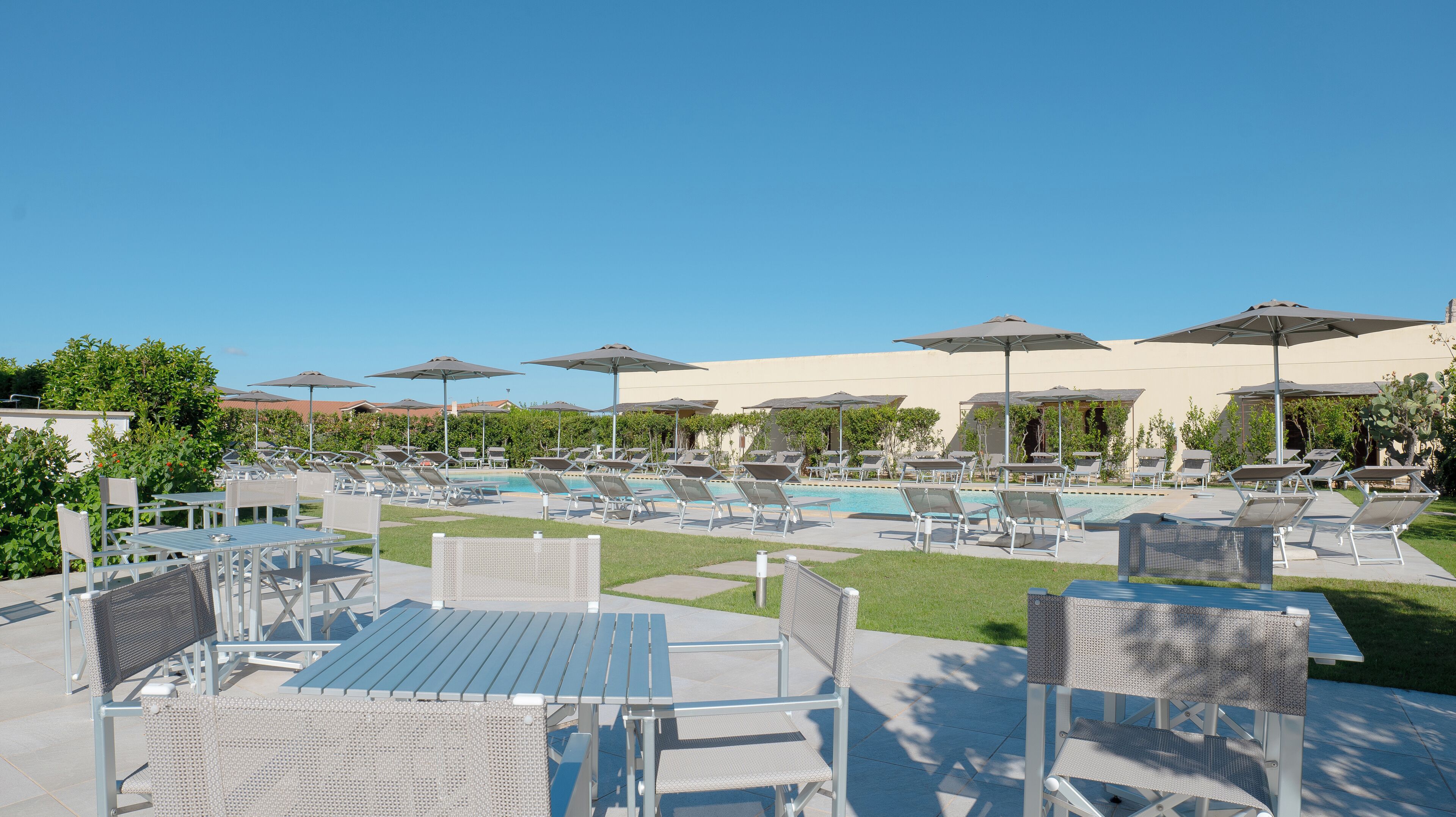 Een zwembadterras met ligbedden en parasols, een zwembad en een terras met tafels en stoelen.