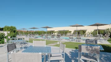 A poolside area with lounge chairs and umbrellas, a pool, and a patio with tables and chairs.