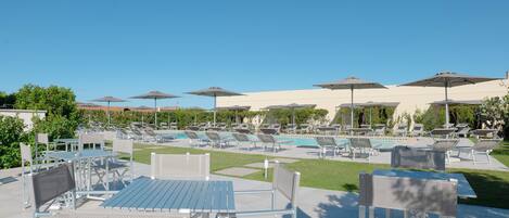 Zona junto a la piscina con sillones de descanso y sombrillas, una piscina y un patio con mesas y sillas.