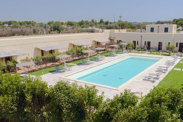 Una piscina con sillas de descanso y sombrillas, rodeada de edificios y vegetación.