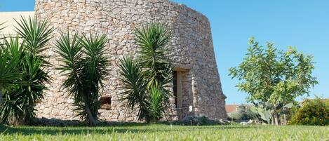 A stone building with a curved facade, surrounded by well-maintained grass and several palm trees.