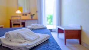 Ein ordentlich bezogenes Bett mit gefalteten weißen Handtüchern, ein Nachttisch aus Holz und ein kleiner Tisch in einem Hotelzimmer mit Fenster und Spiegel an der Wand.