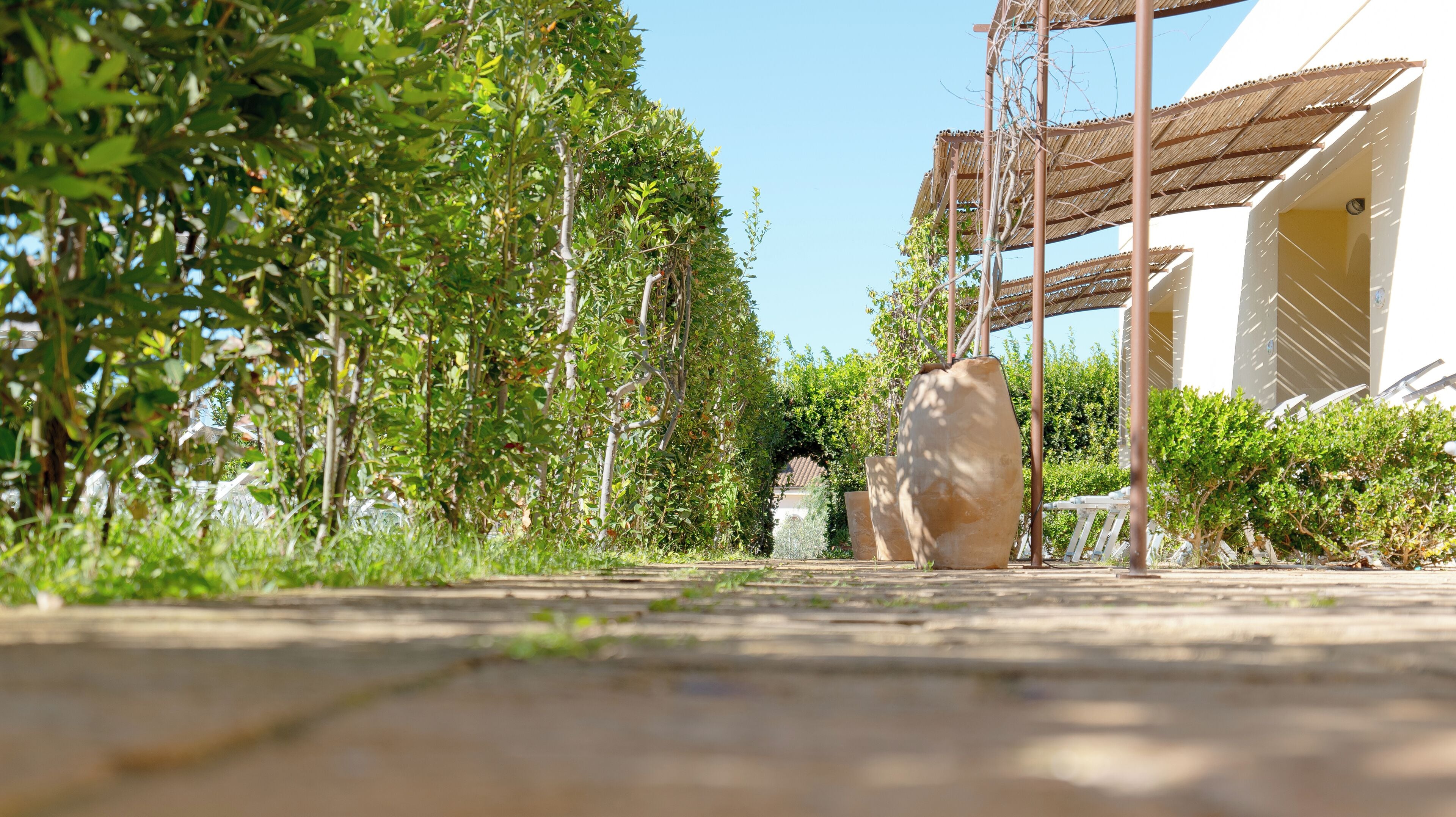 A pathway lined with greenery and a large stone sculpture, leading to a building with a shaded outdoor area.