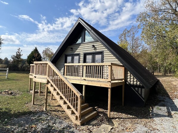 A log cabin with a wooden deck and a staircase leading to a balcony. - Quietly Charming A-Frame (Madisonville)