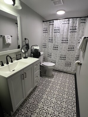 A bathroom with a white sink, black faucets, a toilet, and a shower curtain with text. - Quietly Charming A-Frame (Madisonville)