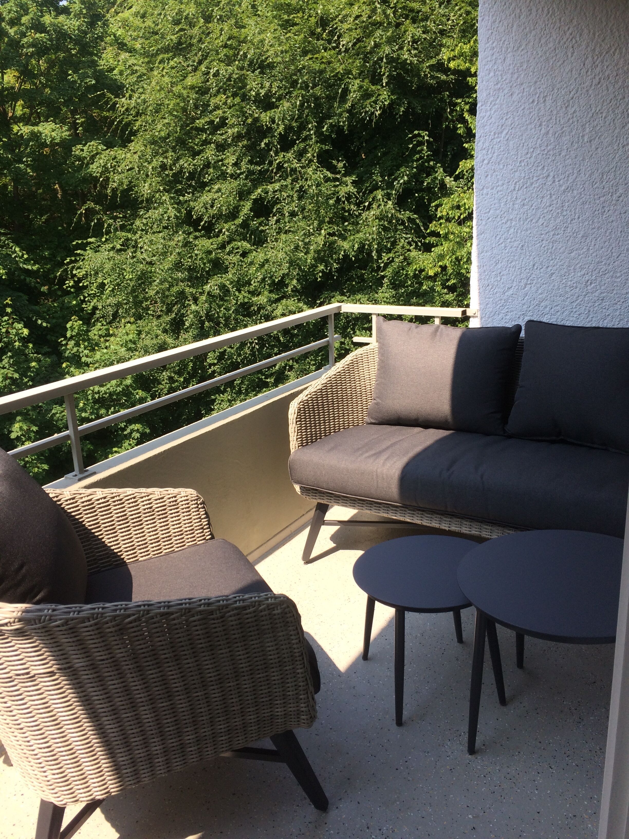 Ein Balkon mit Korbmöbeln, darunter eine Couch und Stühle, sowie ein kleiner Tisch.