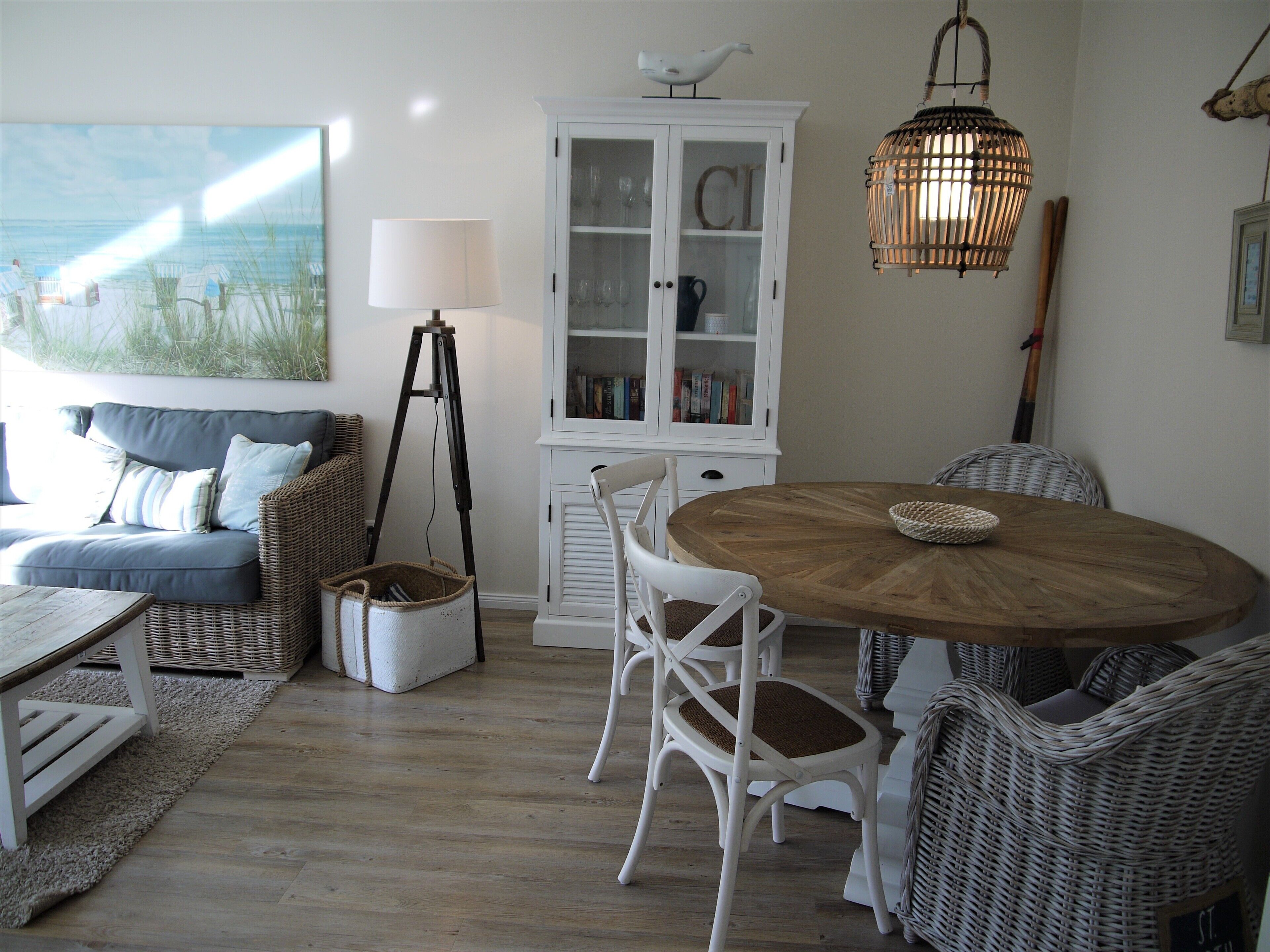 A cozy living room with a sofa, chairs, a wooden dining table, a cabinet, and a painting of a beach scene.