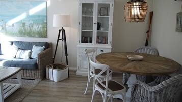 A cozy living room with a sofa, chairs, a wooden dining table, a cabinet, and a painting of a beach scene.