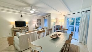 A dining area with a long table, chairs, and a television in the background. - The Olive Shell- condo steps to the beach (St Simons Island)