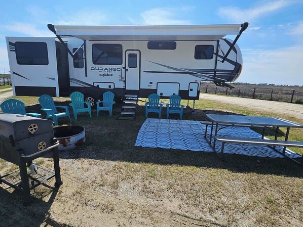 A Durance RV with a covered patio area, outdoor seating, and a grill. - RV15 | Coastal Getaway – Durango Half Ton (Bolivar Peninsula)