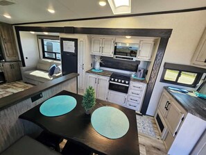 A compact RV kitchen with a dining area, white cabinetry, a stove, and a small seating area. - RV15 | Coastal Getaway – Durango Half Ton (Bolivar Peninsula)