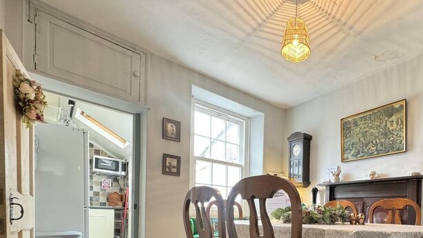 A dining area with a table set for two, a fireplace, and a large window providing natural light. - The Old Locksmith Cottage (Ulverston)