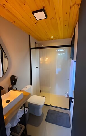 A compact bathroom with a wooden ceiling, a round mirror, a sink, a toilet, and a glass shower enclosure. - Sitio Sunset Joy (Santa Maria)