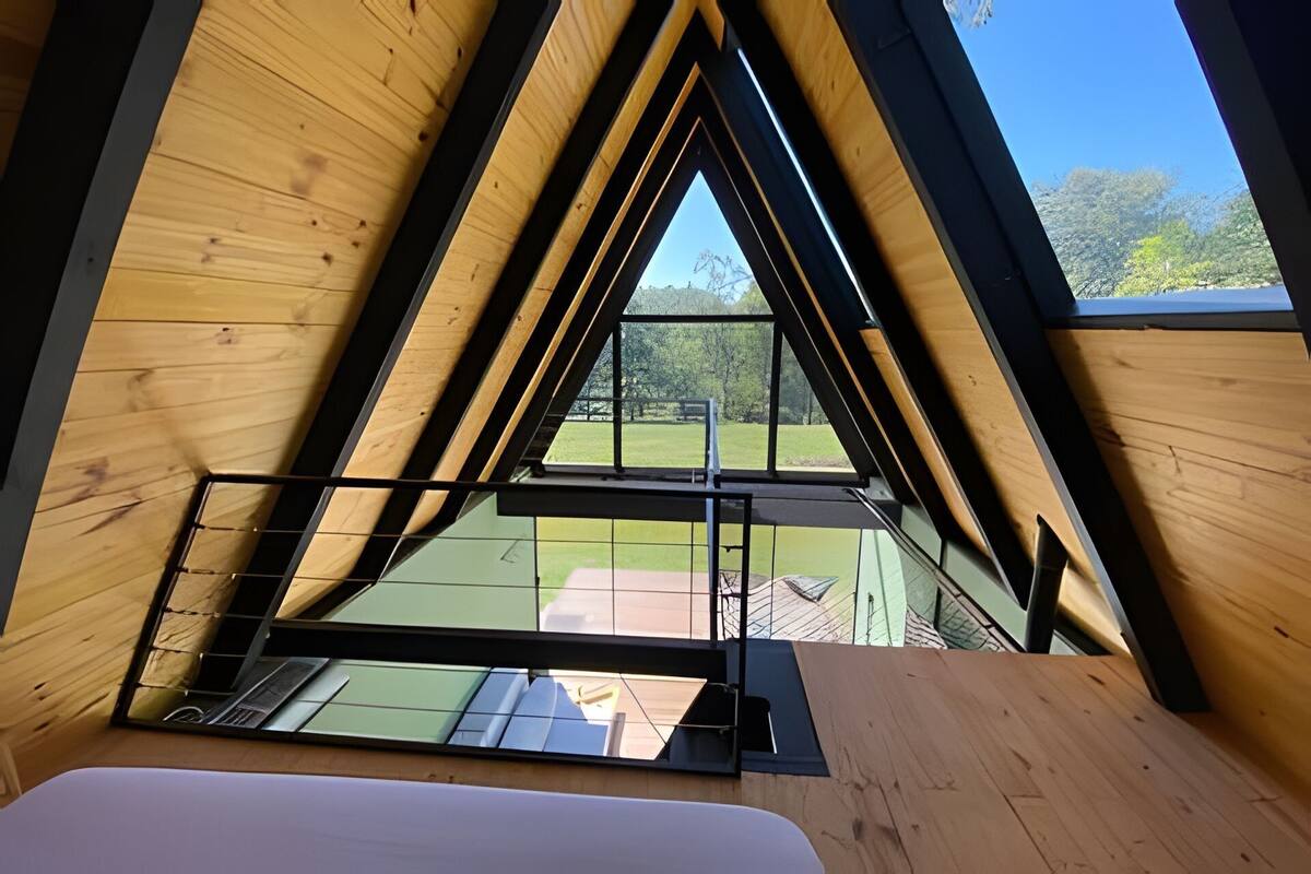 A room with a sloped ceiling and large windows, offering a view of a green landscape.