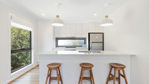 Une cuisine moderne avec des meubles blancs, un réfrigérateur en acier inoxydable, un four encastré et une grande fenêtre donnant sur un paysage verdoyant.