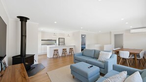 Un salon moderne avec un canapé, un pouf et un meuble pour la télévision. Il y a également un coin cuisine équipé d’une cuisinière et de quelques tabourets.